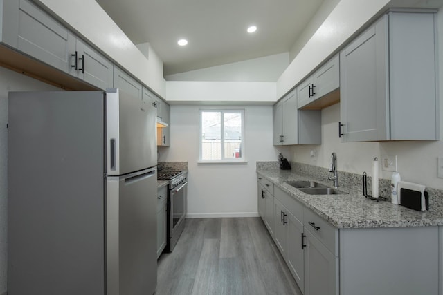 kitchen featuring a sink, light stone counters, appliances with stainless steel finishes, light wood-style floors, and lofted ceiling