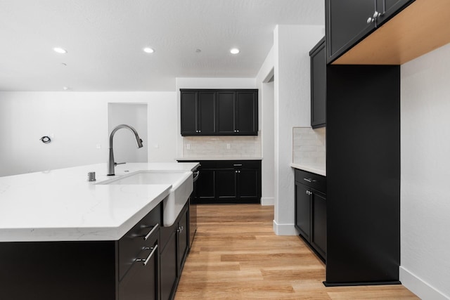 kitchen featuring sink, tasteful backsplash, light stone counters, light hardwood / wood-style floors, and a center island with sink