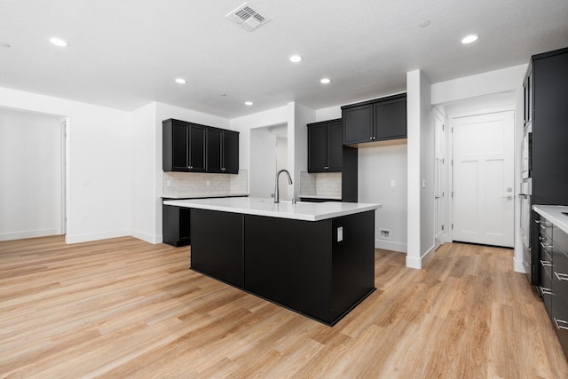 kitchen featuring sink, a center island with sink, backsplash, and light hardwood / wood-style flooring