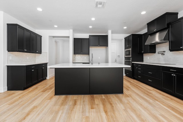 kitchen featuring an island with sink, appliances with stainless steel finishes, sink, and light hardwood / wood-style flooring