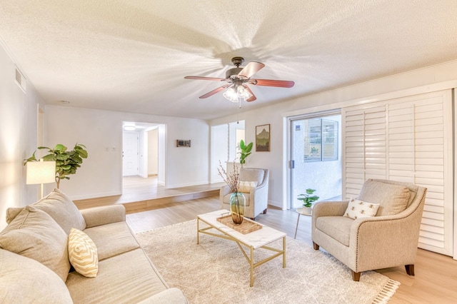 living room with ceiling fan, a textured ceiling, and light hardwood / wood-style flooring