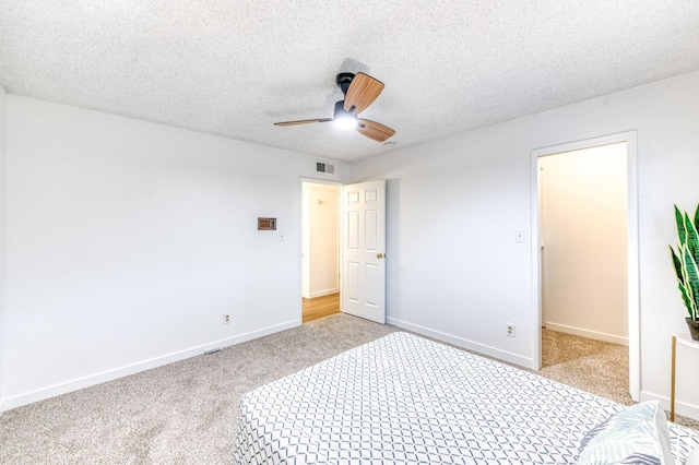 unfurnished bedroom with light carpet, ceiling fan, a walk in closet, and a textured ceiling