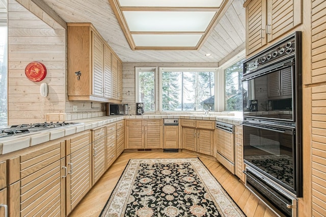 kitchen featuring tile countertops, light wood-type flooring, white gas stovetop, black double oven, and backsplash