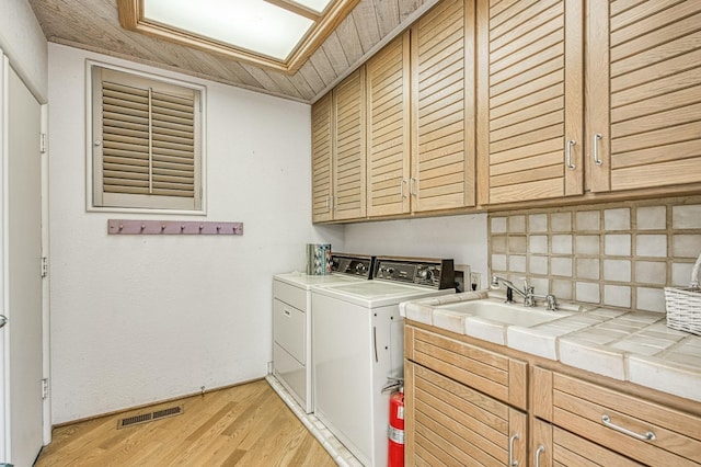 laundry area featuring sink, a skylight, cabinets, light hardwood / wood-style floors, and separate washer and dryer