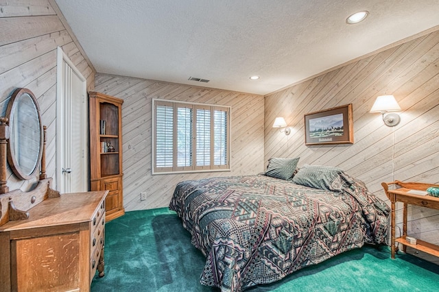 bedroom with wooden walls, a textured ceiling, and dark colored carpet