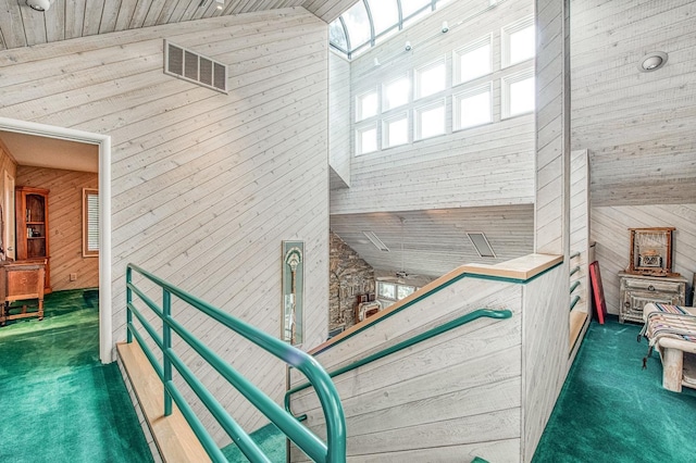 interior space featuring lofted ceiling with skylight, wooden ceiling, dark carpet, and wood walls