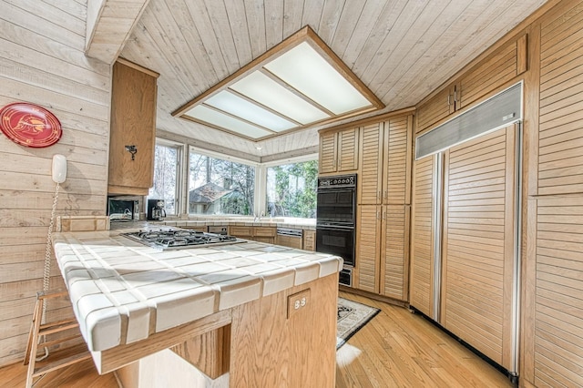 kitchen with a breakfast bar, double oven, tile counters, stainless steel gas cooktop, and kitchen peninsula