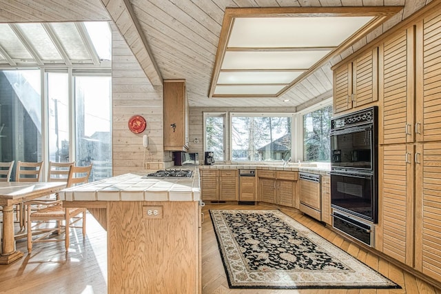 kitchen with wooden walls, black double oven, a center island, stainless steel gas cooktop, and tile counters