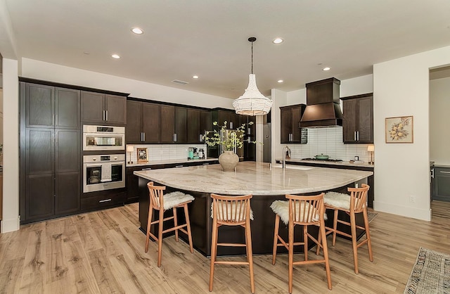 kitchen with light stone countertops, a breakfast bar, a sink, custom range hood, and appliances with stainless steel finishes