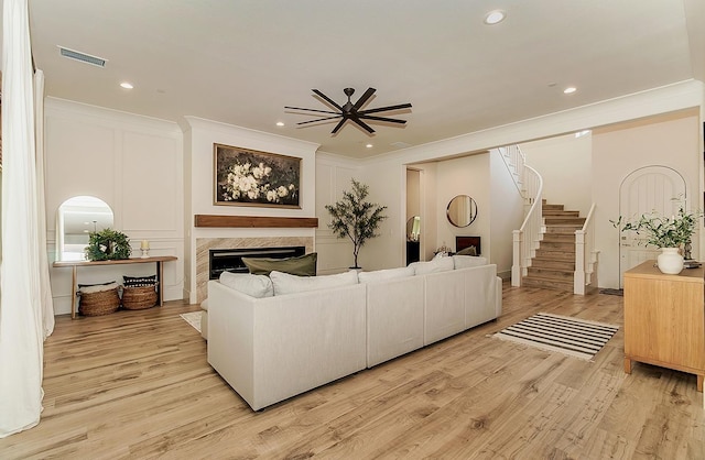 living area with visible vents, ornamental molding, a fireplace, light wood finished floors, and stairs