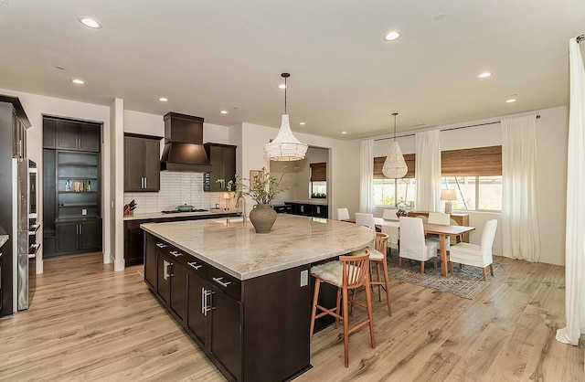 kitchen with light wood-style floors, a kitchen bar, custom range hood, and a kitchen island with sink