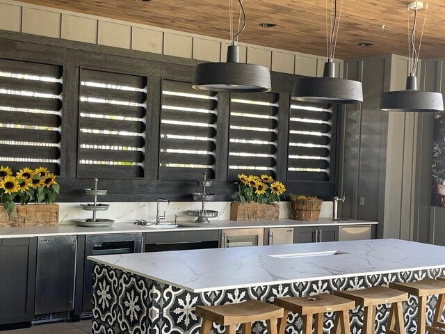 kitchen featuring a sink, light stone counters, dark cabinetry, tile patterned flooring, and wood ceiling