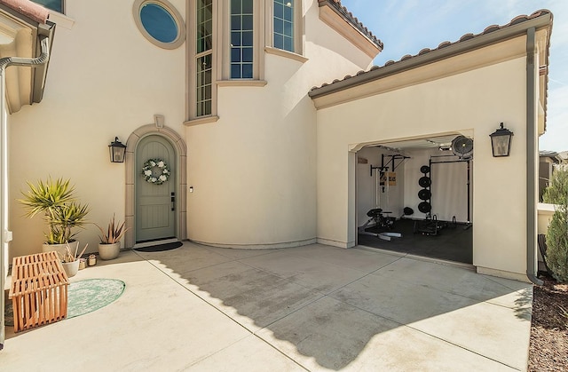 view of exterior entry with stucco siding, driveway, a tile roof, a garage, and a patio area