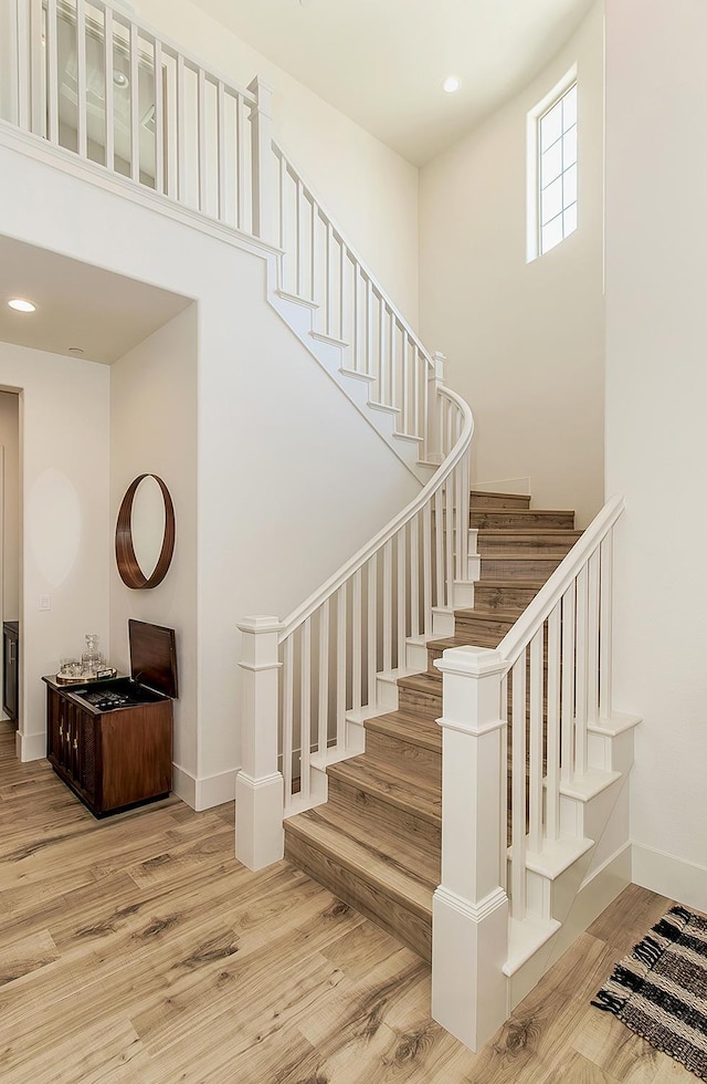 stairway featuring recessed lighting, wood finished floors, baseboards, and a towering ceiling