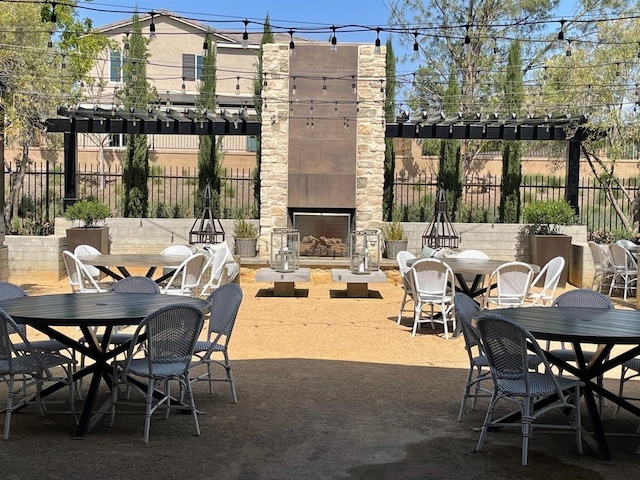 view of patio featuring an outdoor stone fireplace, outdoor dining space, a pergola, and fence