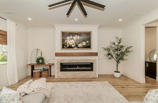 living area with visible vents, a fireplace, light wood-type flooring, and crown molding