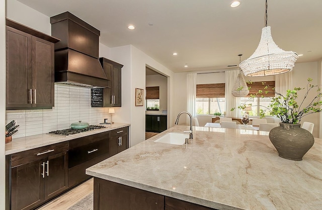 kitchen featuring light stone countertops, stainless steel gas cooktop, a sink, custom range hood, and tasteful backsplash