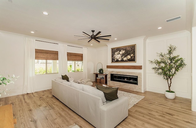 living room with a decorative wall, light wood-type flooring, visible vents, and a premium fireplace