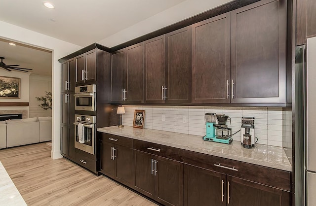 kitchen featuring decorative backsplash, dark brown cabinets, light stone countertops, and light wood finished floors