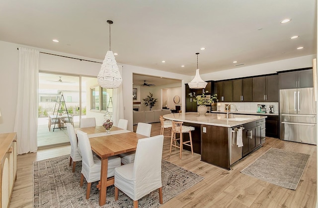 kitchen featuring a sink, tasteful backsplash, light wood-style floors, dark brown cabinetry, and appliances with stainless steel finishes