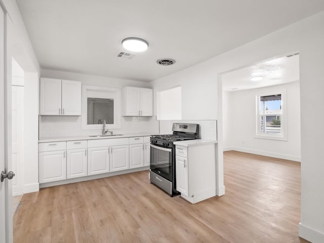 kitchen featuring white cabinetry, sink, decorative backsplash, gas range, and light hardwood / wood-style flooring