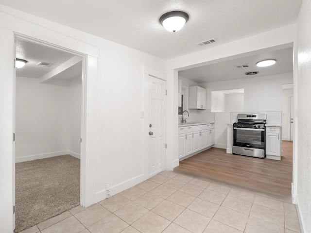 kitchen featuring white cabinetry, sink, stainless steel stove, and light tile patterned floors