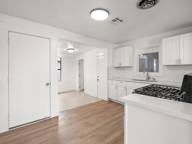 kitchen with white cabinetry, sink, backsplash, light stone counters, and light hardwood / wood-style flooring