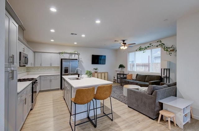 kitchen featuring appliances with stainless steel finishes, sink, a kitchen breakfast bar, a kitchen island with sink, and light hardwood / wood-style flooring