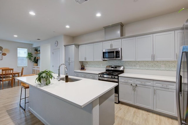 kitchen with sink, backsplash, a kitchen island with sink, light hardwood / wood-style floors, and stainless steel appliances