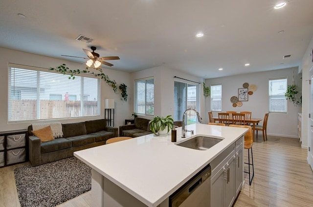 kitchen with sink, light hardwood / wood-style flooring, a breakfast bar, a kitchen island with sink, and stainless steel dishwasher