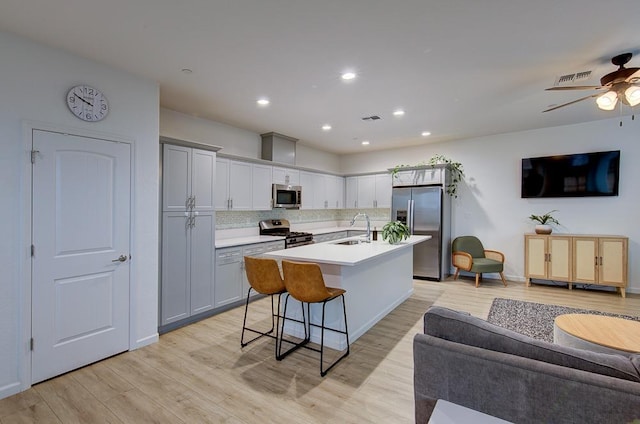 kitchen with appliances with stainless steel finishes, sink, a kitchen bar, a kitchen island with sink, and light hardwood / wood-style floors