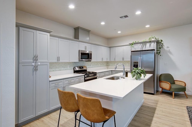 kitchen with sink, light hardwood / wood-style flooring, a breakfast bar area, appliances with stainless steel finishes, and an island with sink