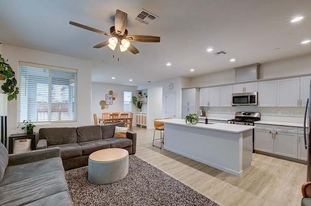 kitchen featuring stainless steel appliances, a kitchen island with sink, decorative backsplash, and light wood-type flooring