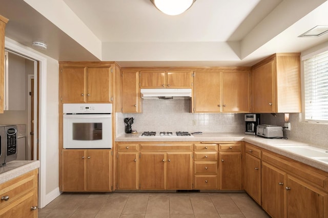 kitchen with tasteful backsplash, light tile patterned floors, and white appliances