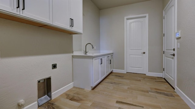 laundry area with electric dryer hookup, sink, light hardwood / wood-style floors, and cabinets