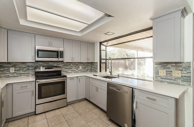 kitchen with sink, light tile patterned floors, appliances with stainless steel finishes, gray cabinets, and backsplash