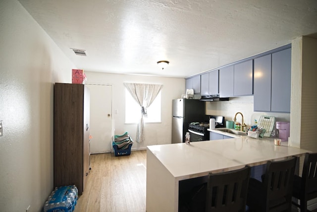 kitchen featuring light countertops, visible vents, light wood-style flooring, gas range, and a peninsula