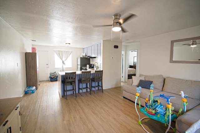 living area featuring light wood-style flooring, a textured ceiling, visible vents, and a ceiling fan