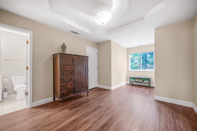 unfurnished bedroom with hardwood / wood-style floors, a tray ceiling, and ensuite bathroom