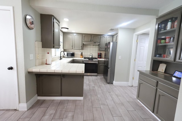 kitchen with sink, tile countertops, appliances with stainless steel finishes, kitchen peninsula, and decorative backsplash