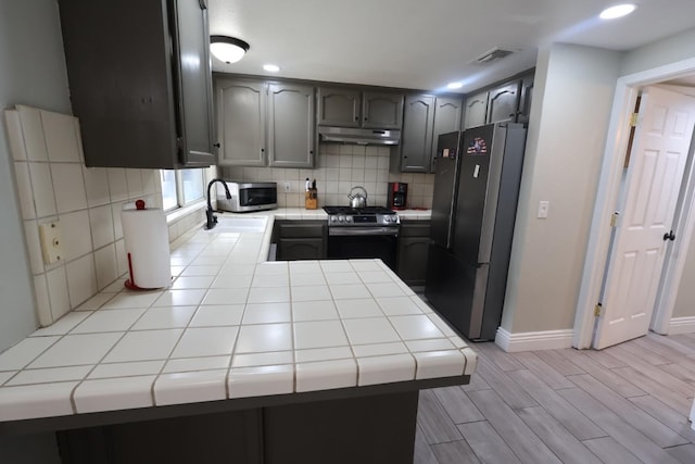 kitchen featuring sink, tile countertops, kitchen peninsula, stainless steel appliances, and backsplash