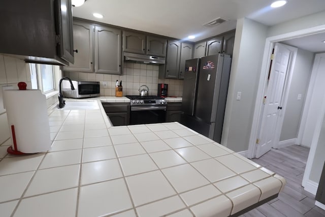 kitchen with appliances with stainless steel finishes, sink, tile counters, and decorative backsplash