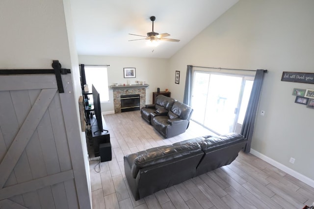 living room featuring ceiling fan, a barn door, a stone fireplace, and a wealth of natural light