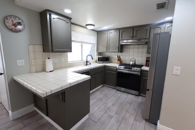 kitchen featuring sink, appliances with stainless steel finishes, decorative backsplash, tile countertops, and kitchen peninsula