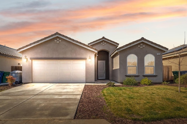 mediterranean / spanish-style house featuring a garage, driveway, a lawn, and stucco siding