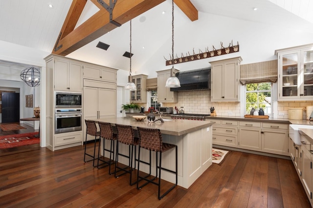 kitchen featuring a kitchen island with sink, hanging light fixtures, built in appliances, custom exhaust hood, and cream cabinetry
