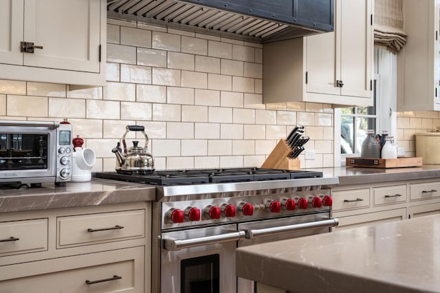 kitchen with range with two ovens, premium range hood, white cabinetry, and decorative backsplash
