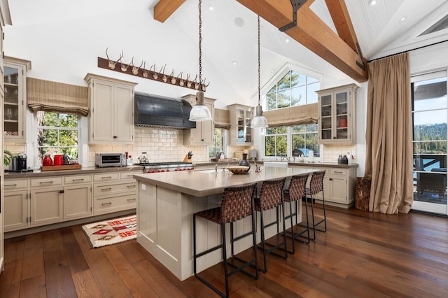 kitchen with decorative light fixtures, a center island with sink, a kitchen breakfast bar, custom range hood, and cream cabinetry