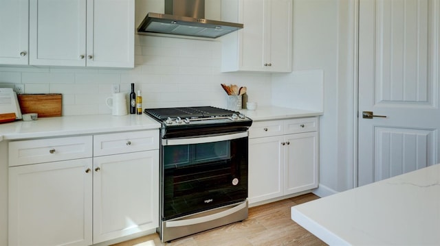 kitchen featuring stainless steel range with gas cooktop, tasteful backsplash, white cabinets, wall chimney exhaust hood, and light hardwood / wood-style flooring