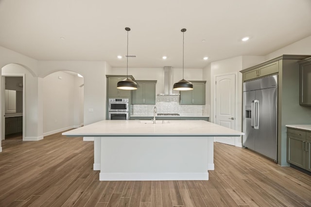 kitchen featuring stainless steel appliances, light stone countertops, pendant lighting, and wall chimney exhaust hood